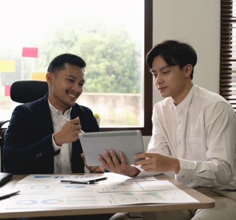 Asian business adviser meeting A group of executives in suits discussing around a conference table with charts and laptops, emphasizing C level succession in a professional boardroom setting.