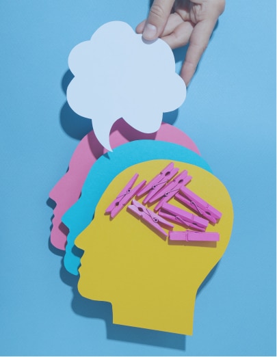Pict 1 A person's head, made of yellow paper, with pink clothespins inside, representing different thoughts. A hand holds a blank thought bubble above the head. Behind the yellow head are blue and pink paper silhouettes of other people's heads.