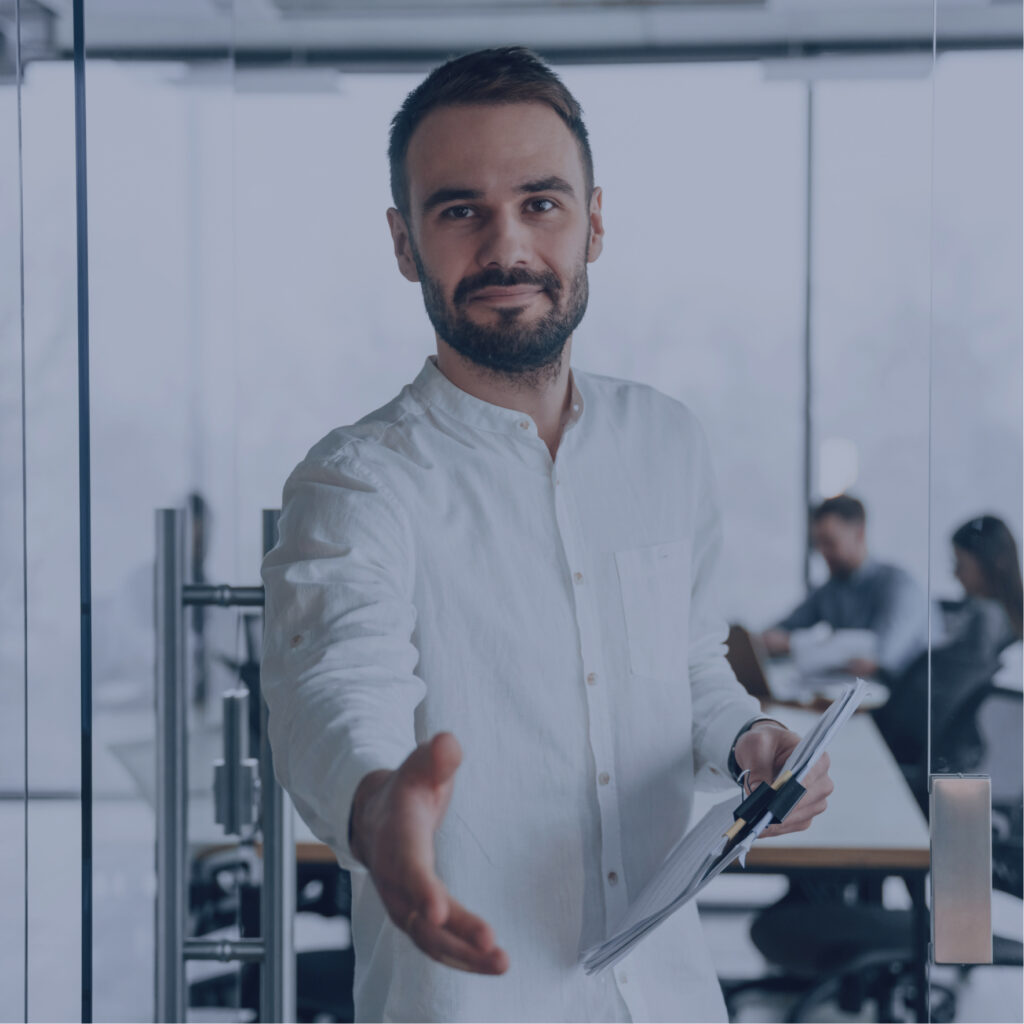 TB 14 Seorang pria berpakaian putih berjabat tangan sambil memegang dokumen di kantor modern, menggambarkan transformasi kepemimpinan dengan suasana profesional di latar belakang.