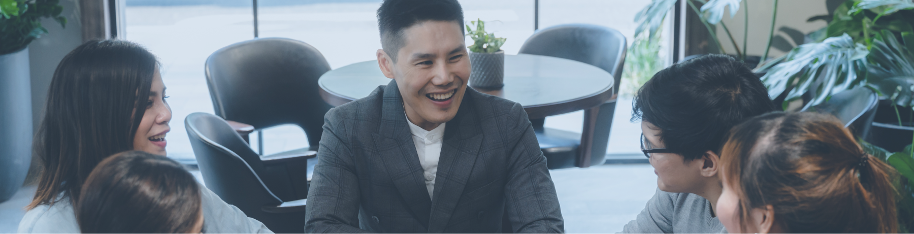 Banner Performance Enhancement Seorang pria berjas abu-abu tersenyum lebar sambil berjabat tangan dengan rekan di meja rapat modern, dikelilingi tim muda yang antusias di ruang kerja cerah dengan tanaman hijau. Suasana mencerminkan Increased Performance melalui kolaborasi dan semangat tinggi.