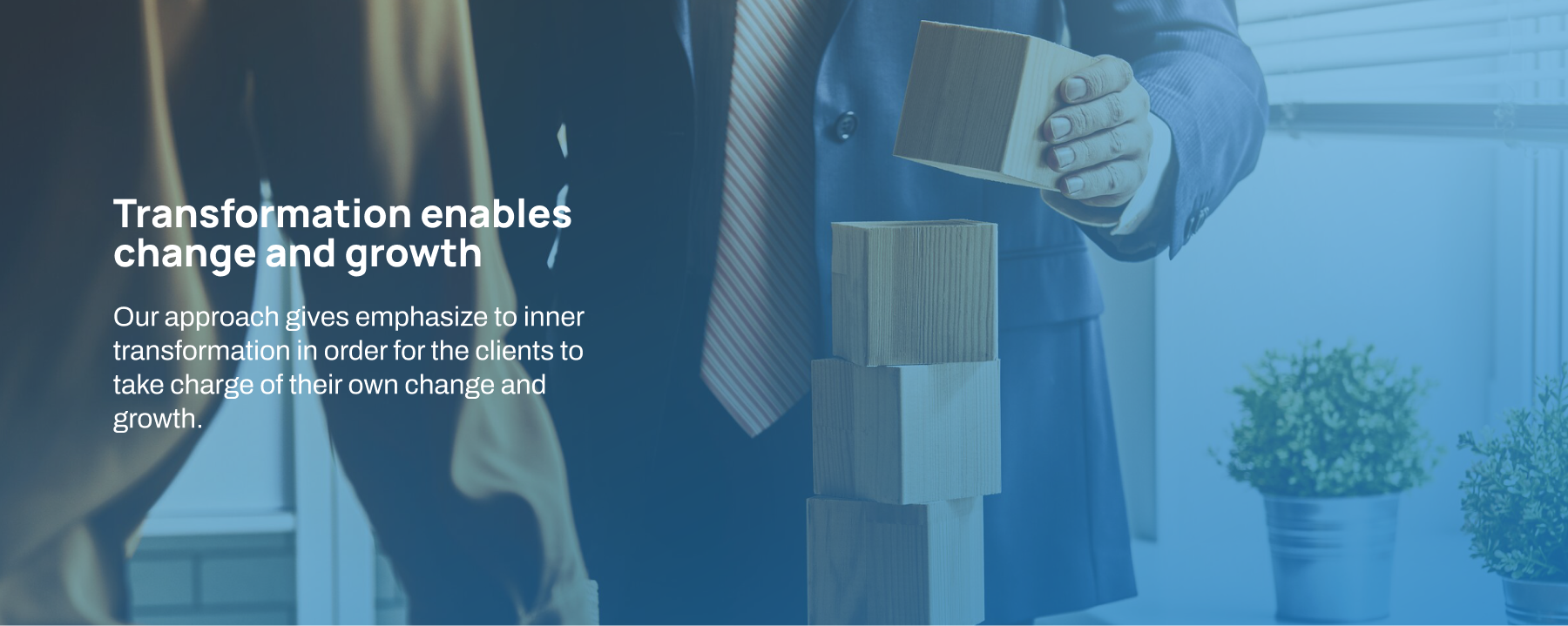 Homepage banner 2 A person in a suit holding wooden blocks, with text about transformation enabling change and growth through an inner-focused approach, relating to coaching Indonesia for personal and professional development.